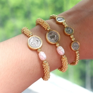 Detail of layered gold beaded bracelets with baroque pearls and religious medal pendants
