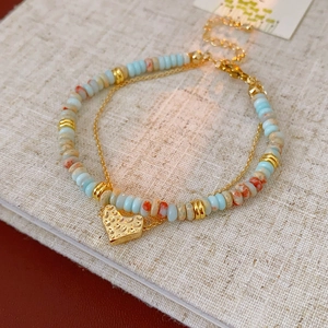 Detail of double-layer beaded bracelet with light blue stone beads and golden heart pendant