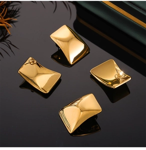 Macro detail of polished 18K gold rectangular earrings on reflective black surface