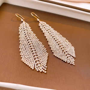 Detailed close-up of golden feather tassel earrings with shimmering inlaid crystals