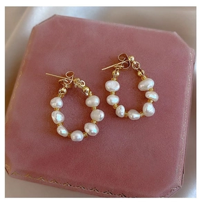 Primer plano de aretes de perlas de agua dulce en caja de terciopelo rosa y detalles en oro