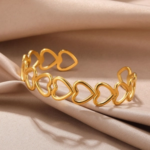 Detail shot of a golden hollow heart-shaped open bangle on elegant champagne satin fabric