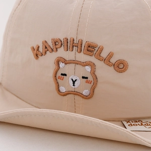 Detail of baby sun hat with bear embroidery and KAPIHELLO text on soft beige fabric