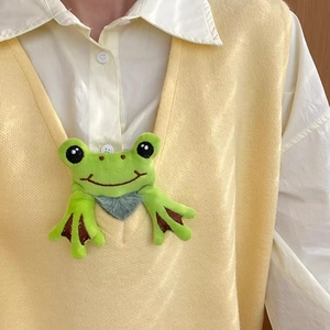 Cute green plush frog hair tie accessory shown as a quirky charm on a yellow knitted vest