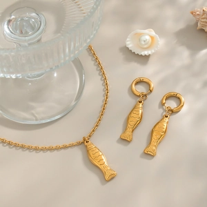 Elegant gold fish pendant necklace and earring set displayed with soft shadows