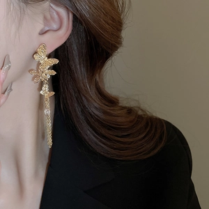 Detailed view of long gold butterfly tassel earrings with crystals on a model