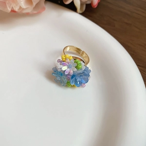 Dettaglio ravvicinato di anello con perline in resina floreale e fascia dorata aperta