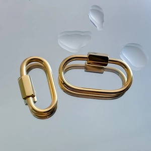 Close-up of gold-plated oval screw clasps with polished finish on reflective water background