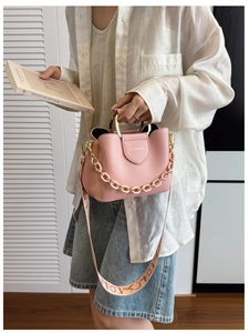 Detail view of pink bucket bag with gold handle and patterned wide strap on a model