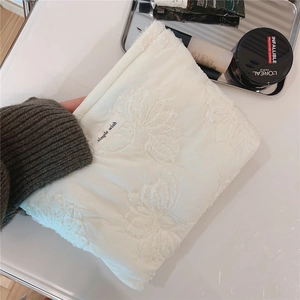 Detail of white quilted clutch bag featuring elegant 3D floral embroidery and soft fabric