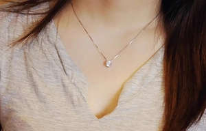 Close-up of a rose gold zircon solitaire pendant on a thin box chain worn on the neck