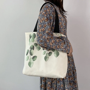 Detail of canvas tote bag with green leaf print and durable black fabric shoulder straps
