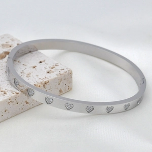 Silver stainless steel bangle with sparkling zircon heart patterns on a stone base