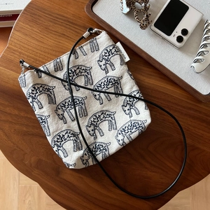 Macro detail of cream canvas crossbody bag featuring navy blue leopard embroidery and simple tag
