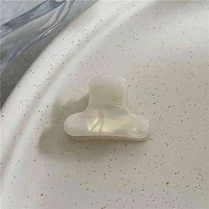 Close-up of a mini pearl white acetate hair claw clip on a beige ceramic plate