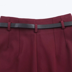 Detail of wine red high waist trousers featuring a slim black belt and fine stitching