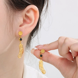 Gros plan détaillé des boucles d'oreilles plume dorées avec pierres noires sur un modèle