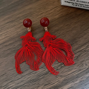Detail of red hollow goldfish earrings with beads on a dark wood background texture