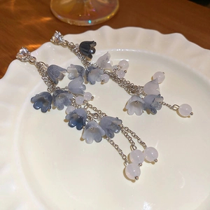 Détail de boucles d'oreilles muguet bleu-gris sur un plateau en céramique blanc