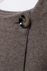Close-up of a glossy dark button on a textured brown knit wool blend coat neckline