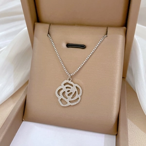 Gros plan du pendentif fleur de camélia en argent mat dans un écrin élégant beige