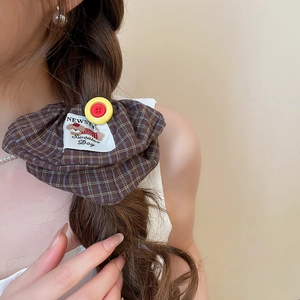 Detail of a brown plaid scrunchie with yellow button and dog label on braided hair