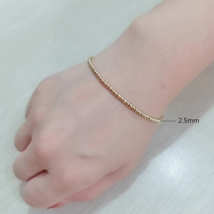 Detail showing a 2.5mm gold beaded stretch bracelet made of stainless steel on wrist
