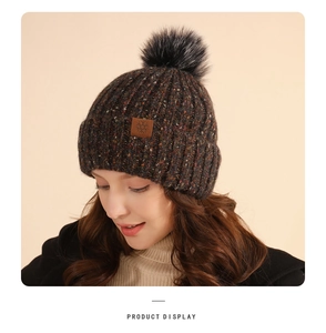 Close-up of a dark brown knit beanie featuring a faux fur pompom and snowflake leather patch