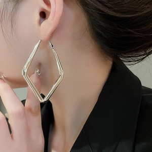 Close-up of a large silver geometric rhombus hoop earring worn by a model in a side view
