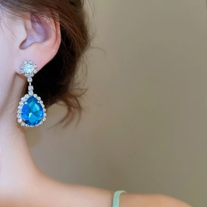 Dettaglio dell'orecchino a goccia blu con alone di diamanti indossato da una modella