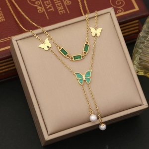 Detail of layered gold necklace featuring emerald green butterfly pendant and white pearls