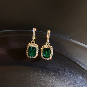 Macro shot of gold earrings with green rectangle gemstones and crystal accents