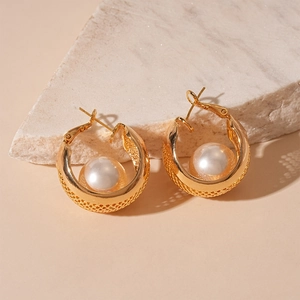 Macro detail of gold-plated mesh hoop earring with a large pearl on a textured block