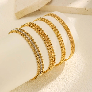 Layered gold and silver stainless steel beaded bracelets on white cylindrical display stand