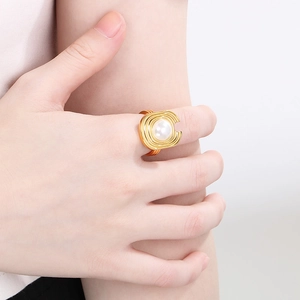 Detail of layered gold geometric rings with white pearl accents on model hand