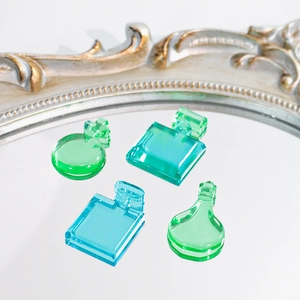 Dettaglio di quattro ciondoli in resina a forma di profumo blu e verdi su specchio