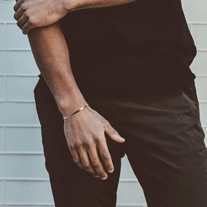 Close-up of a minimalist silver cuff bracelet on a male wrist against a white wall