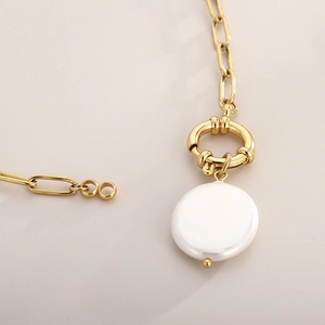 Macro detail of golden rectangular chain link and white baroque pearl charm on a necklace