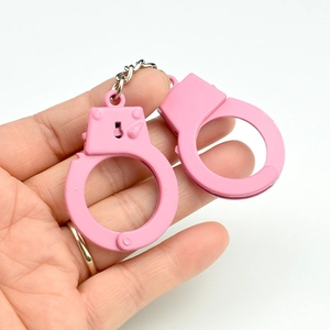 Close-up of a pink miniature metal handcuff keychain toy held in a hand on white background