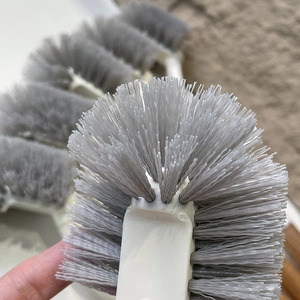Gros plan des poils gris denses et du manche en plastique blanc d'une brosse de toilette