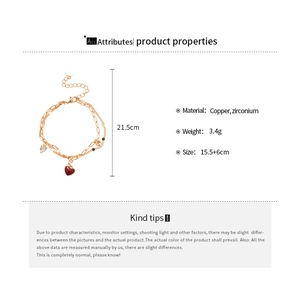 Detail view showing a double-layered gold bracelet with red heart and zircon charms