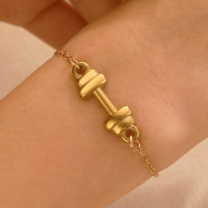 Detailed close-up of a golden dumbbell pendant on a braided black leather cord bracelet