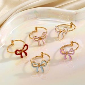 Colorful bow-shaped enamel rings in gold stainless steel on an iridescent tray