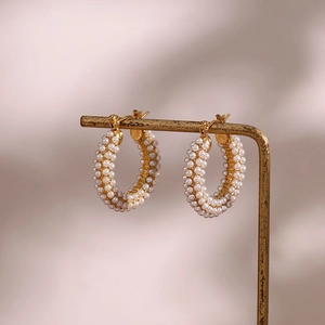 Detail of 18K gold-plated hoop earrings featuring micro-paved white pearls on a stand