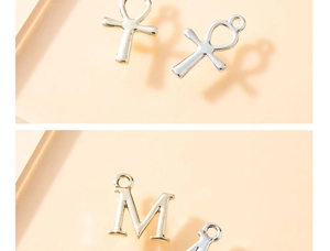 Close-up of golden Ankh and letter M alloy pendants for DIY jewelry crafting