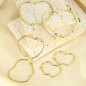 Three pairs of golden heart-shaped hoop earrings in various sizes on silk and stone