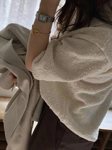 Detail shot of a minimalist 925 silver knot heart bracelet with textured beige knit top
