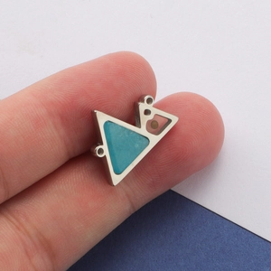 Macro shot of geometric stainless steel pendant with turquoise and bead held by fingers