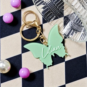 Close-up of a light green butterfly resin keychain with white Lilian name engraving