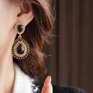 Gros plan de boucles d'oreilles vintage dorées avec gemmes noires portées par un modèle